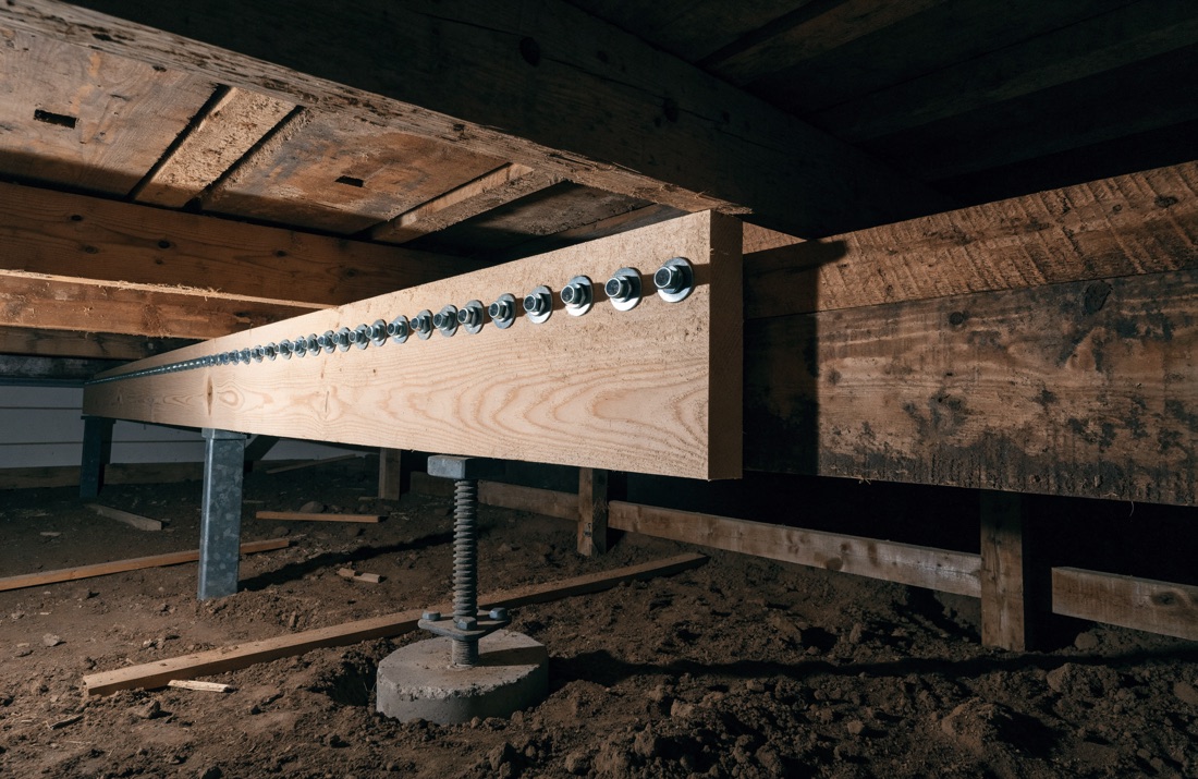 A new joist sistered alongside a damaged one in a crawl space and bolted through, with a temporary support post underneath